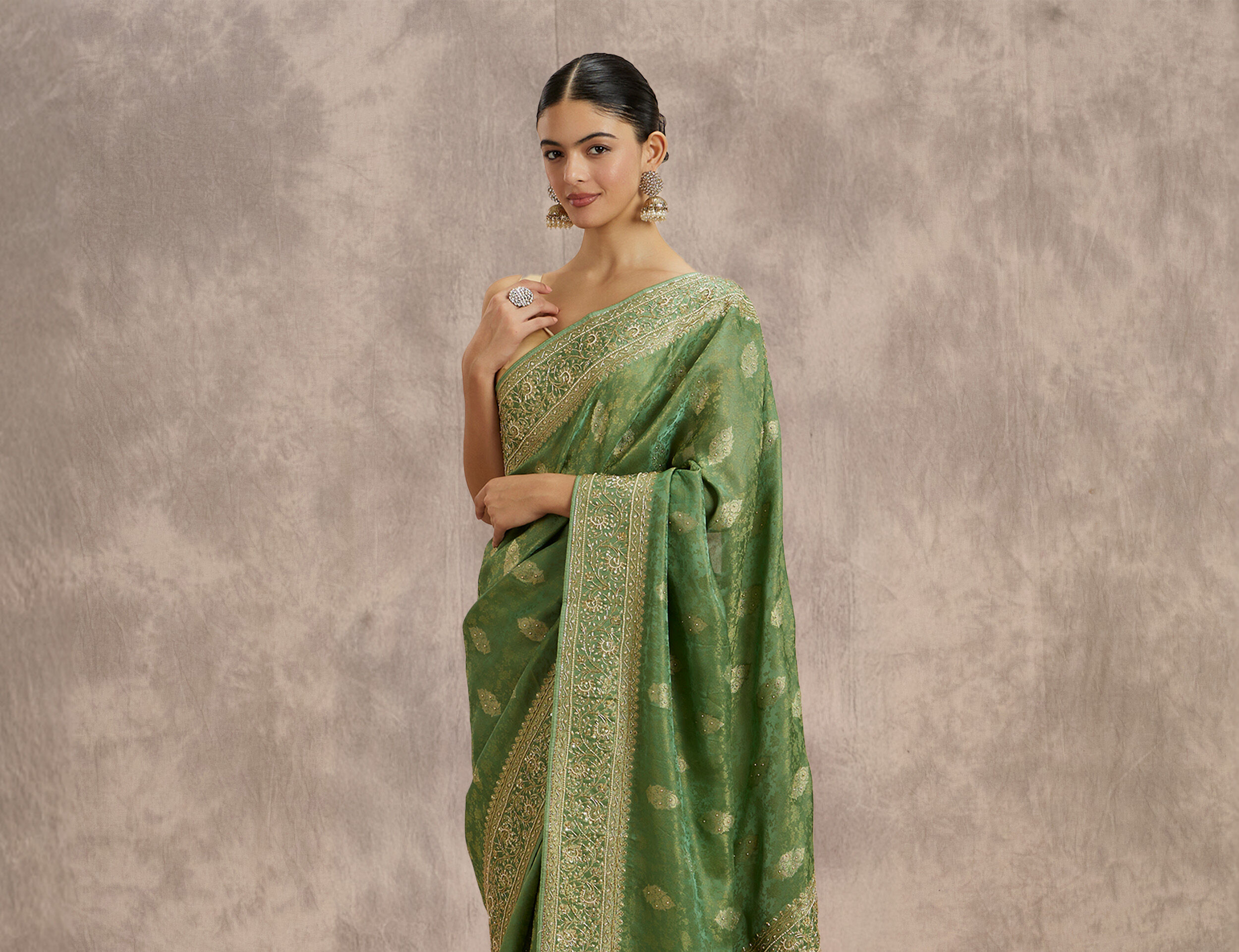 Woman dressed in an olive green Banarasi silk saree with gold zari work, highlighting traditional festive attire.